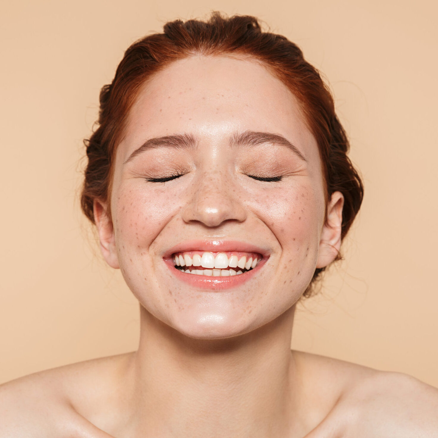 Portrait of a laughing pretty happy smiling amazing young redhead woman posing isolated over beige wall background.